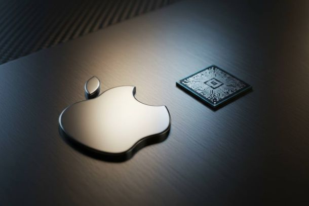 Shiny metallic Apple logo beside a square circuit chip on a dark brushed metal surface.